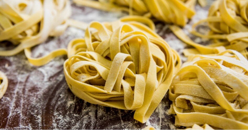 Someone making homemade ravioli on a flour covered counter. Also on the counter is a scooper filled with flour