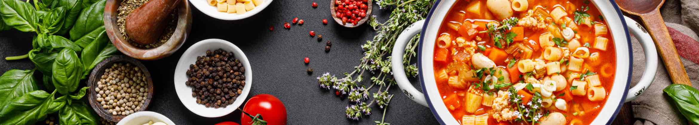 A pot of pasta e fagioli. Next to it on the counter are fresh herbs. 