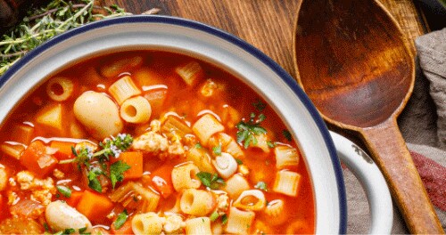 A pot of pasta e fagioli. Next to it on the counter are fresh herbs. 