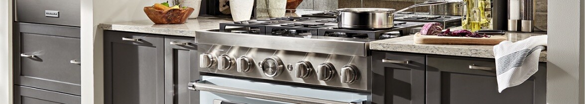 Cuisinière bicombustible KitchenAid avec une casserole sur le rond avant, légume rouge sur une planche à découper sur le comptoir