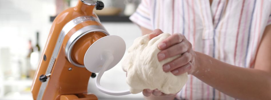 A baker extracts kneaded dough from a mixing bowl that was combined using a KitchenAid Stand Mixer dough hook.