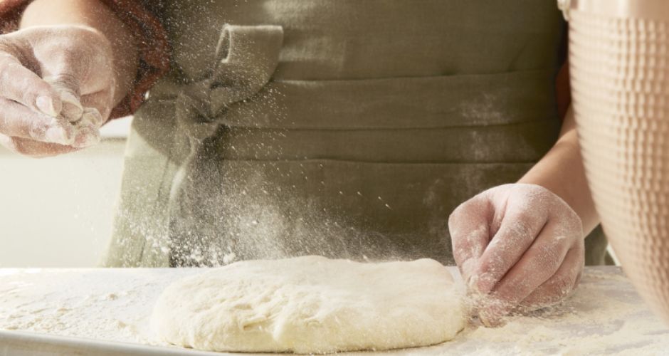 A person is captured sprinkling flour over the dough in preparation for the upcoming rolling process.