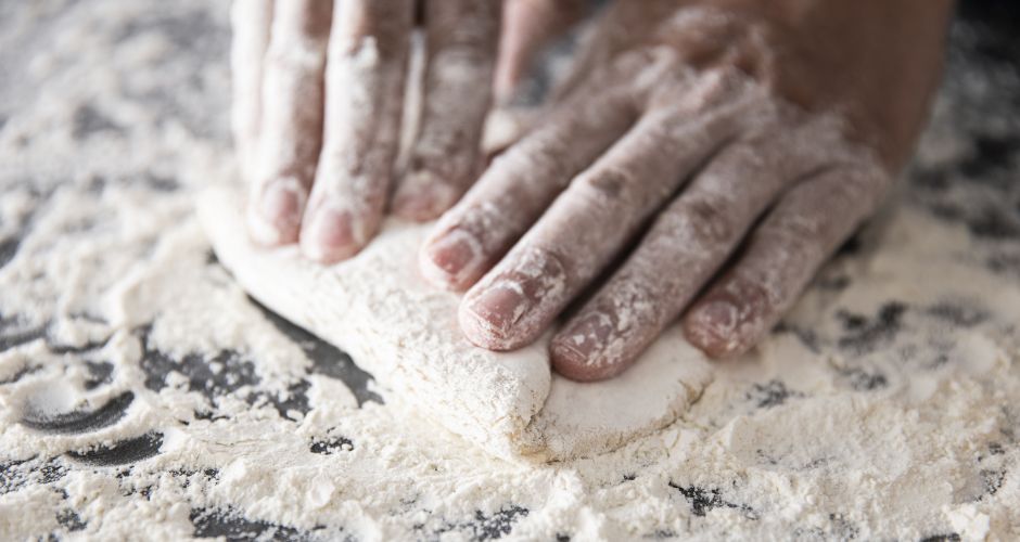 In this close-up image, hands are captured rolling out dough with precision and care.