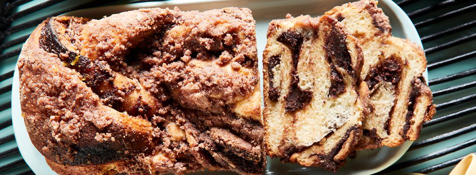 A porcelain platter presents a striking loaf of Babka with its end adorned by precisely cut slices.