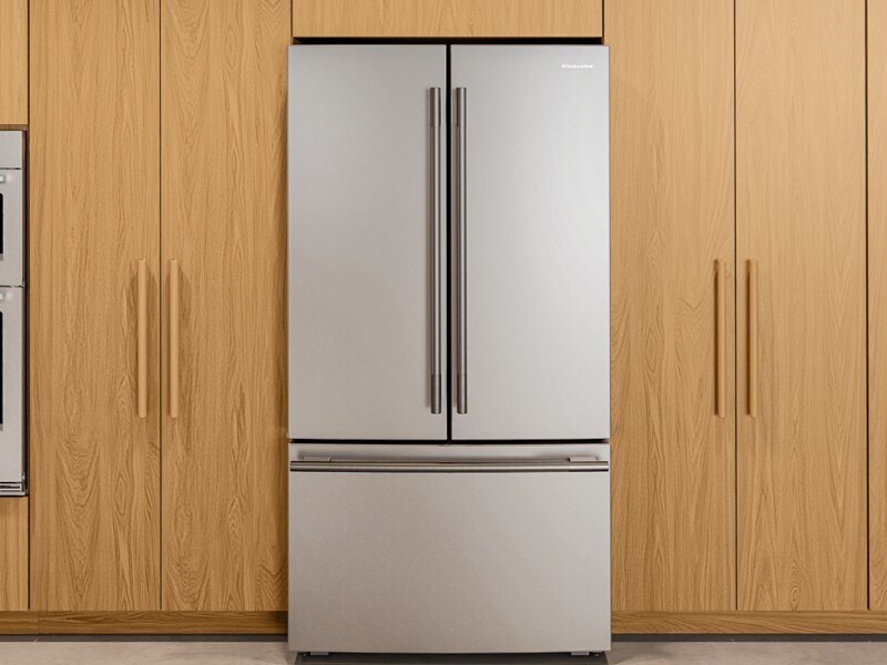 A KitchenAid French door refrigerator surrounded by wooden cabinetry and next to a KitchenAid double wall oven. 