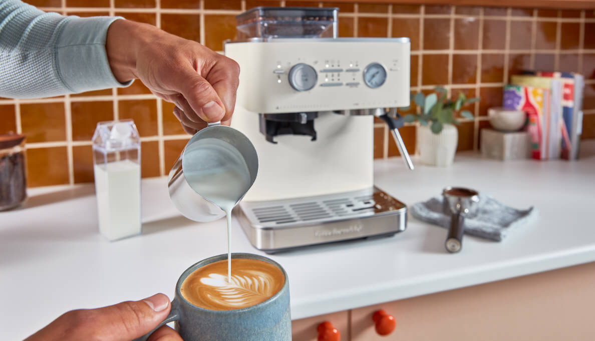 A person pouring steamed milk into an espresso drink.