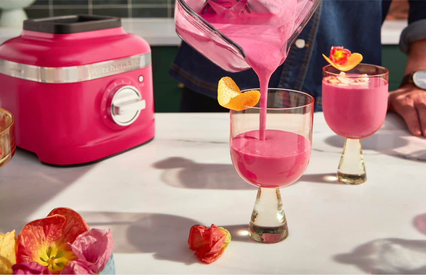 Une personne versant une boisson mélangée à l'hibiscus dans des verres élégants et modernes avec des garnitures florales.