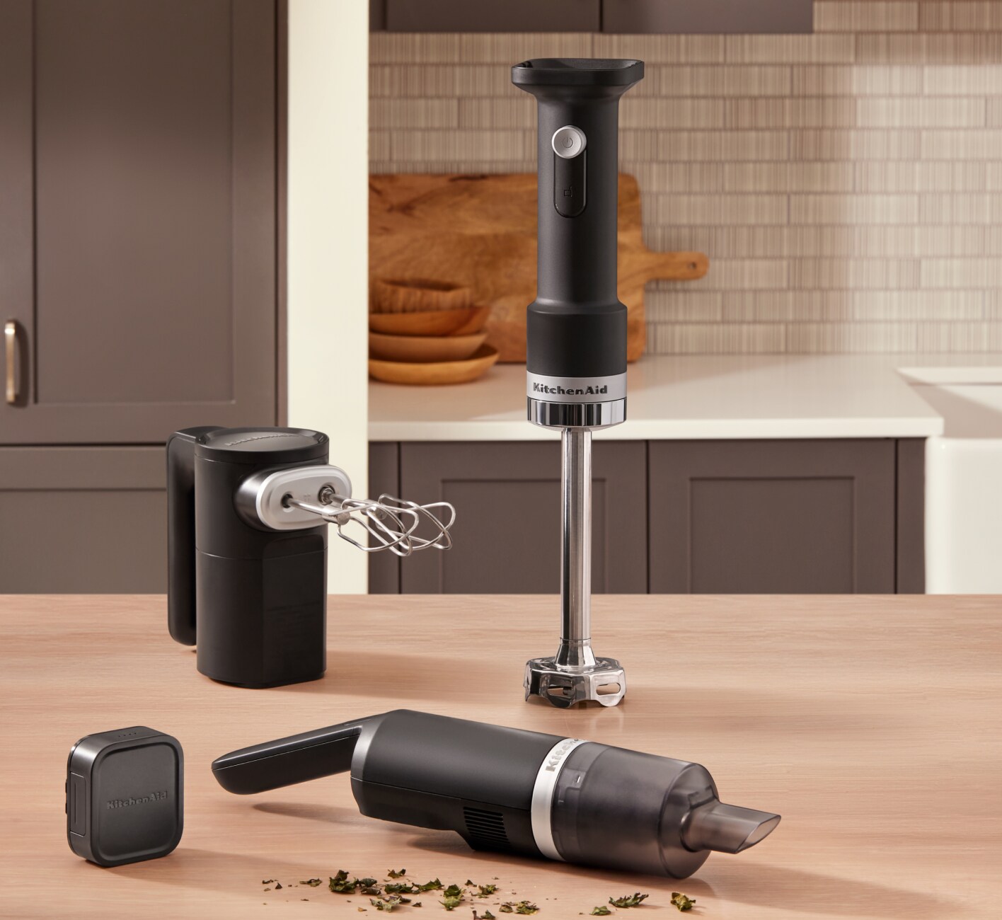 Le batteur à main, le mélangeur à main et l'aspirateur de cuisine sans fil KitchenAid® Go™ sur un comptoir à côté d'herbes sèches