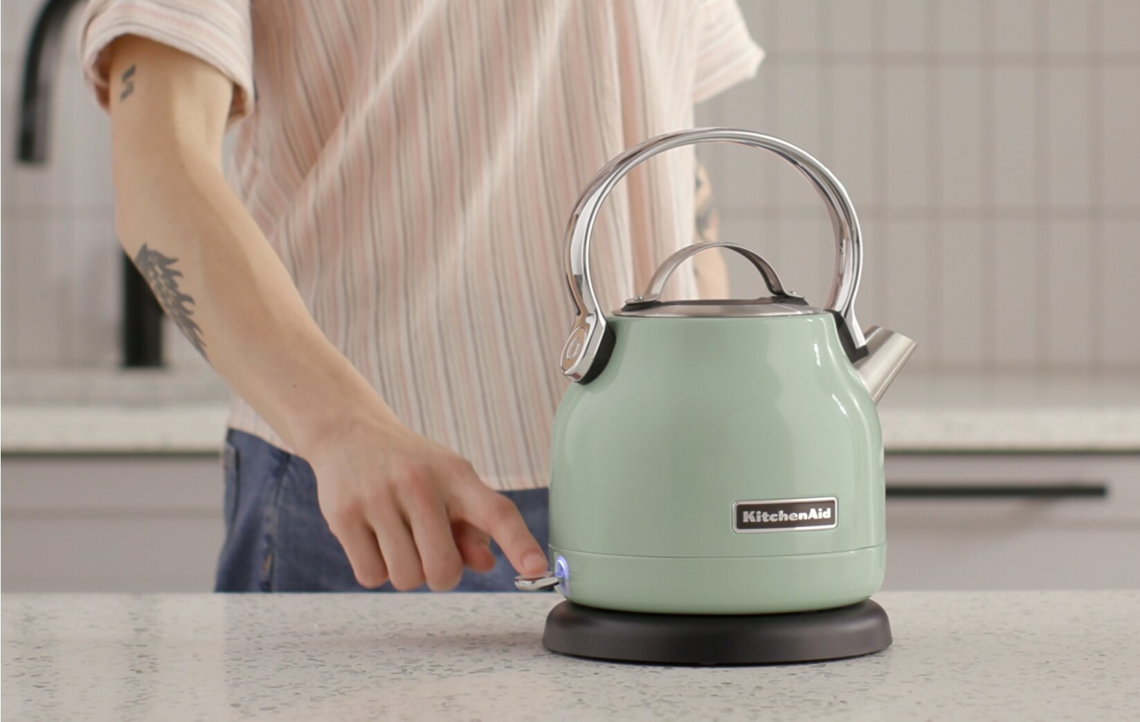 A pistachio KitchenAid® electric kettle next to two drinks on a countertop.