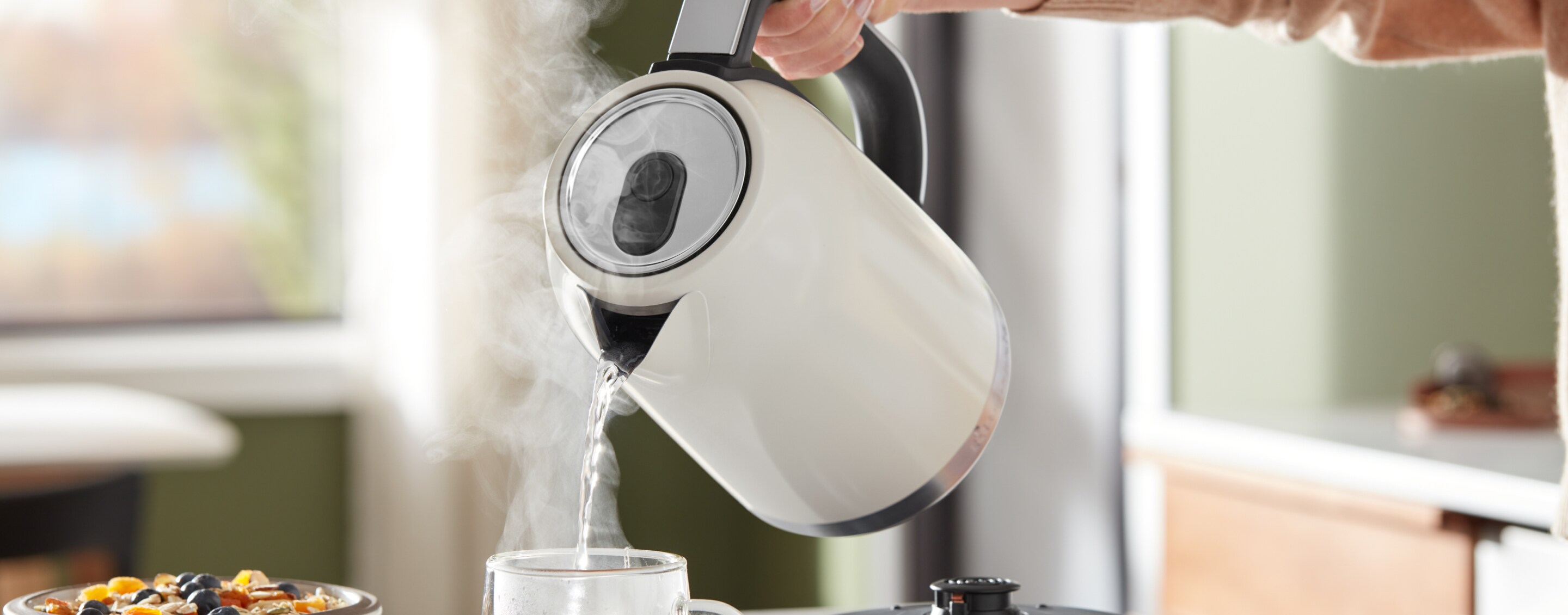 A KitchenAid® kettle pouring hot water into a glass mug.