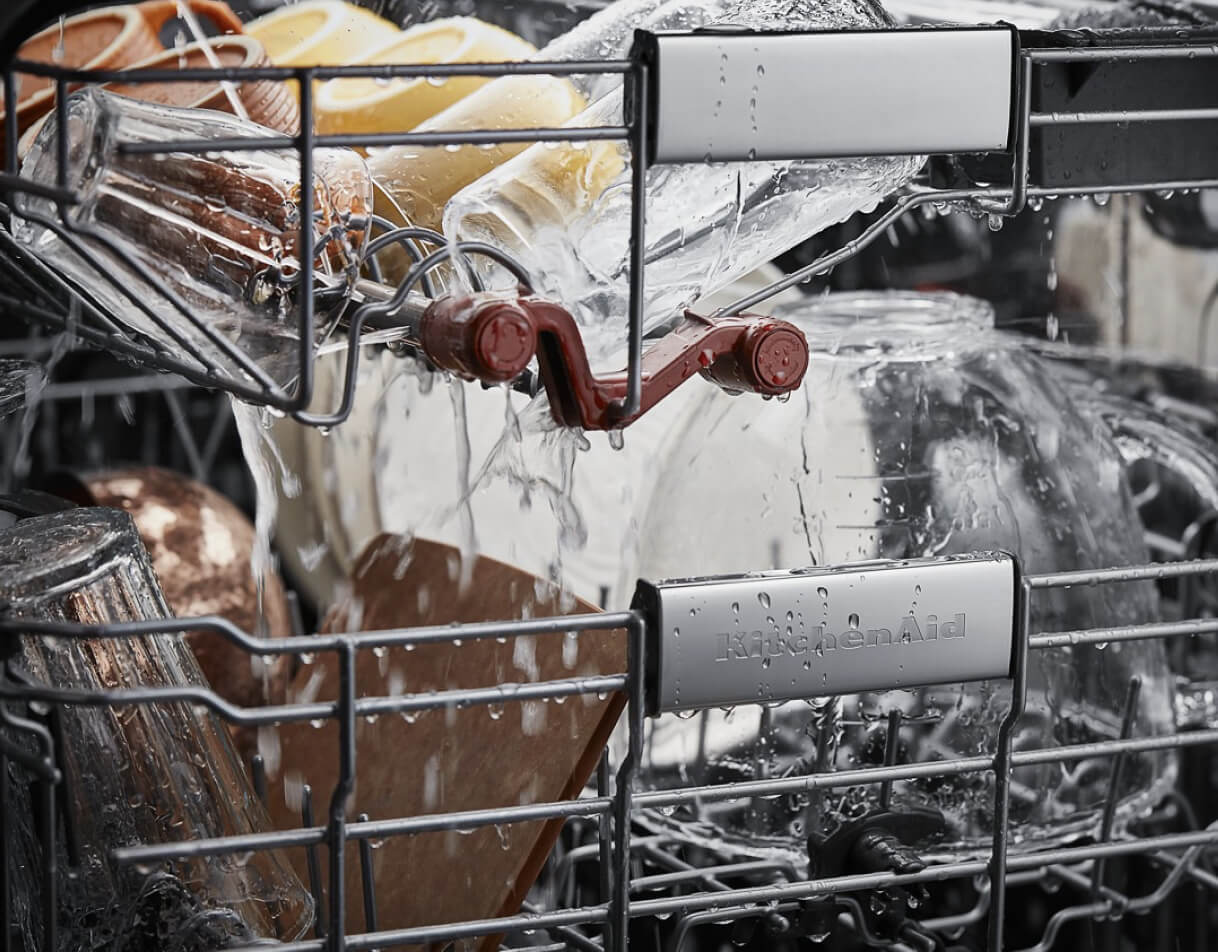 The interior of a KitchenAid Dishwasher that's in the middle of a wash cycle. The items being washed includes glassware.