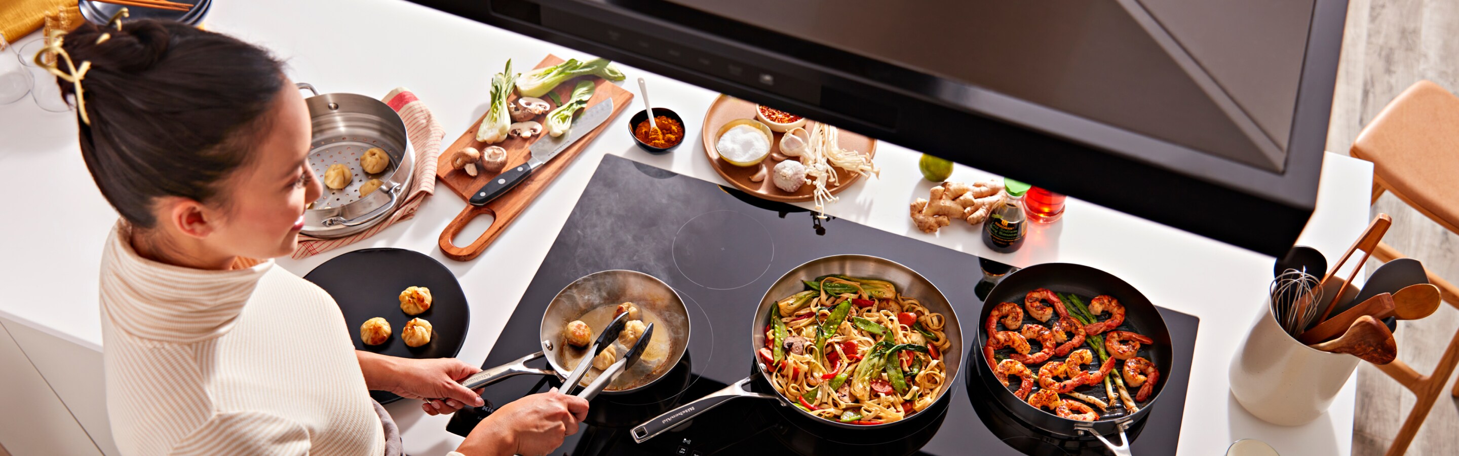 A person cooking on a KitchenAid® cooktop.