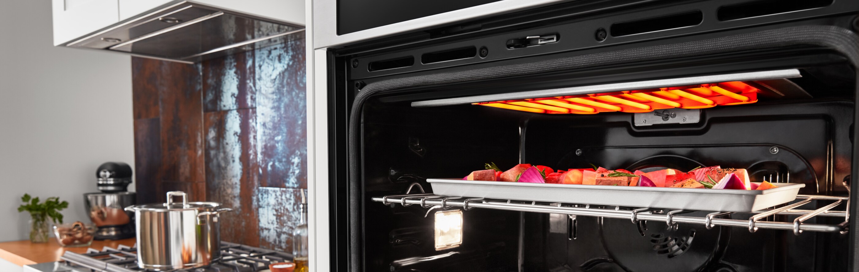Assorted vegetables on a sheet pan broiling in an open wall oven