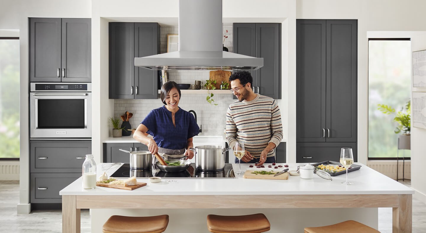 Two people cooking at a kitchen island over a cooktop