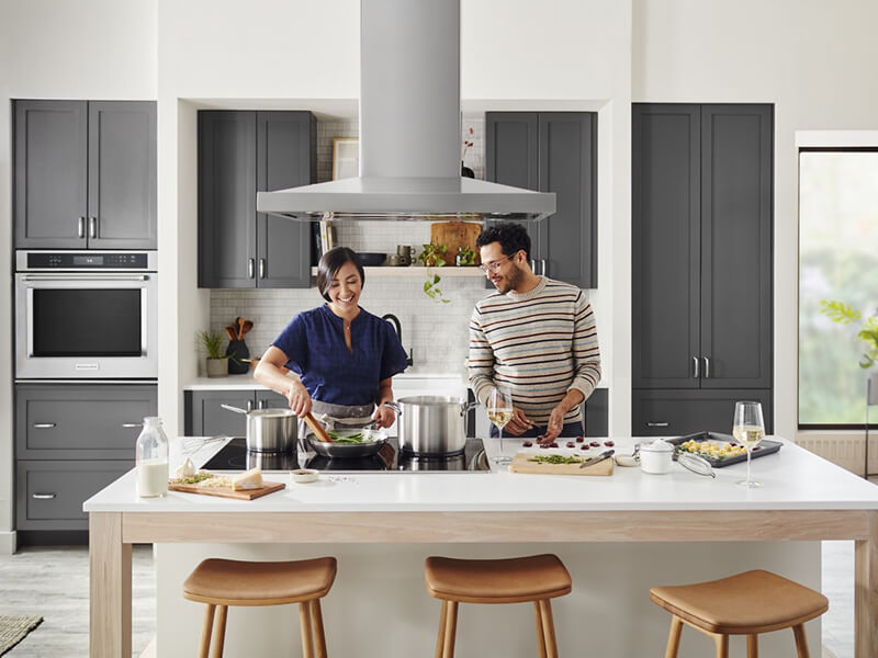 Two people cooking at a kitchen island over a cooktop