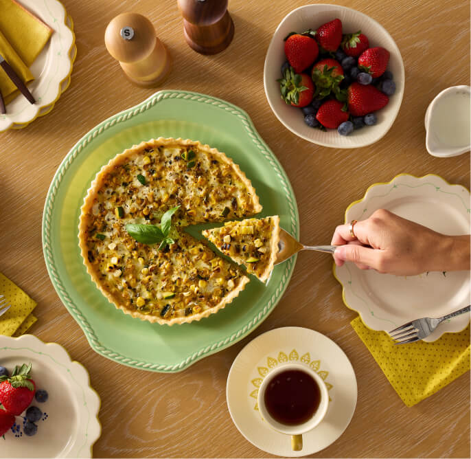 On a table is a quiche with a slice being removed, a cup of coffee, a bowl of strawberries and blueberries, salt and pepper shakers and a few other items.