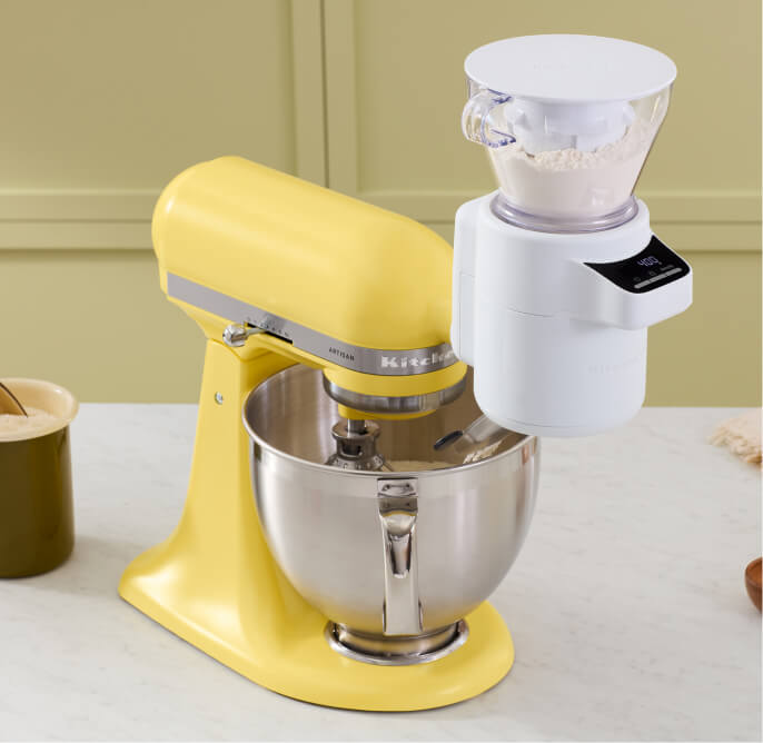 On a counter is a Butter KitchenAid Stand Mixer with a Sifter + Scale Attachement. 