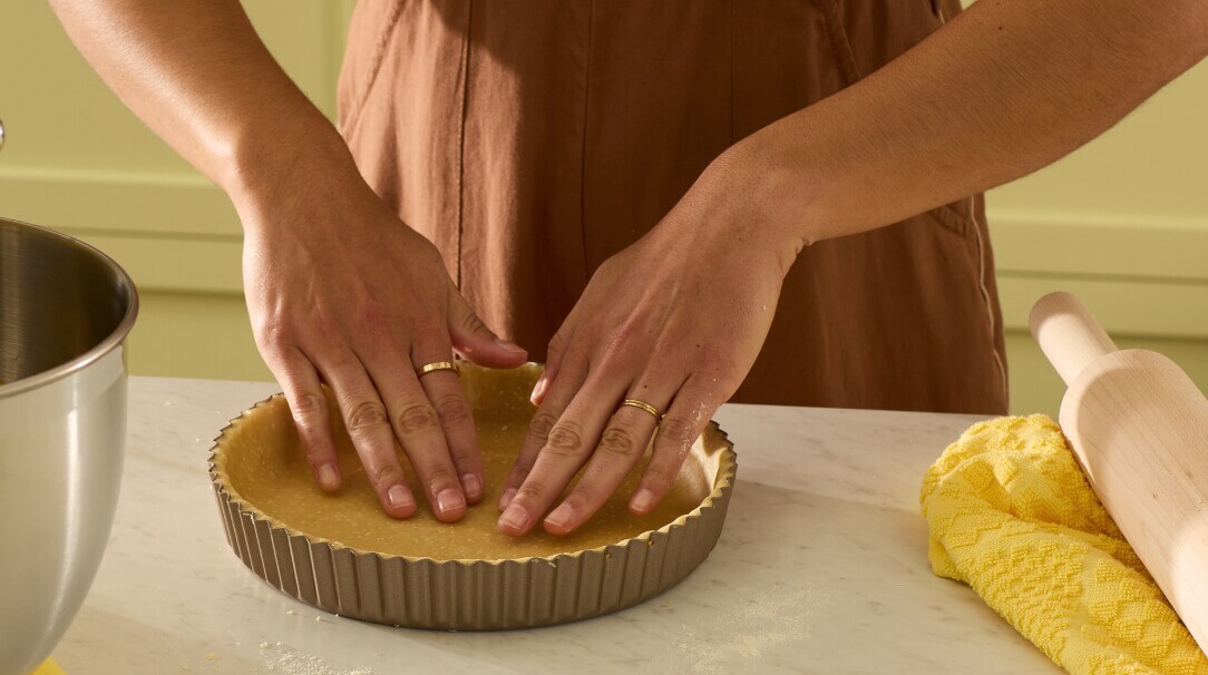 A person pressing a quiche crust into a tart pan.