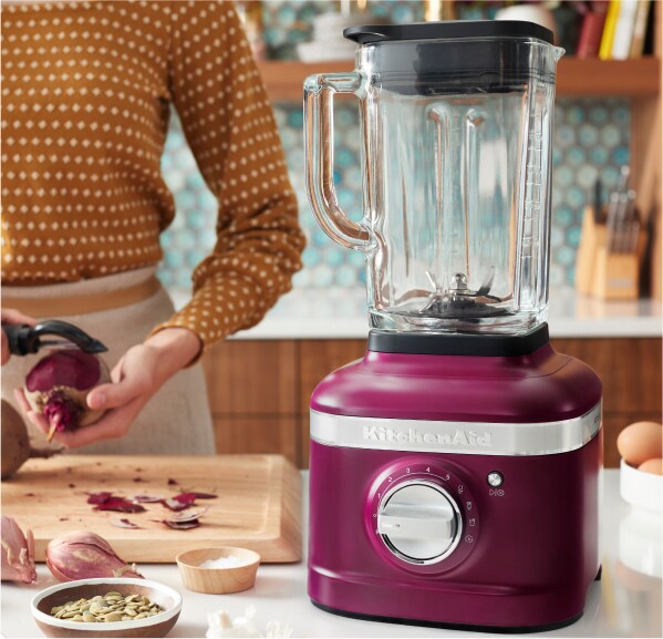 Une personne épluchant une betterave à l'arrière-plan d'un batteur sur socle de la couleur de l’année KitchenAid, Betterave