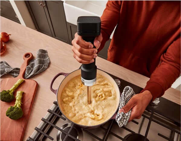 Une personne utilisant le mélangeur à main sans fil KitchenAid Go™ pour mélanger de la soupe dans un faitout.