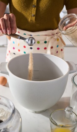 A person adding yeast to a KitchenAid bread bowl.