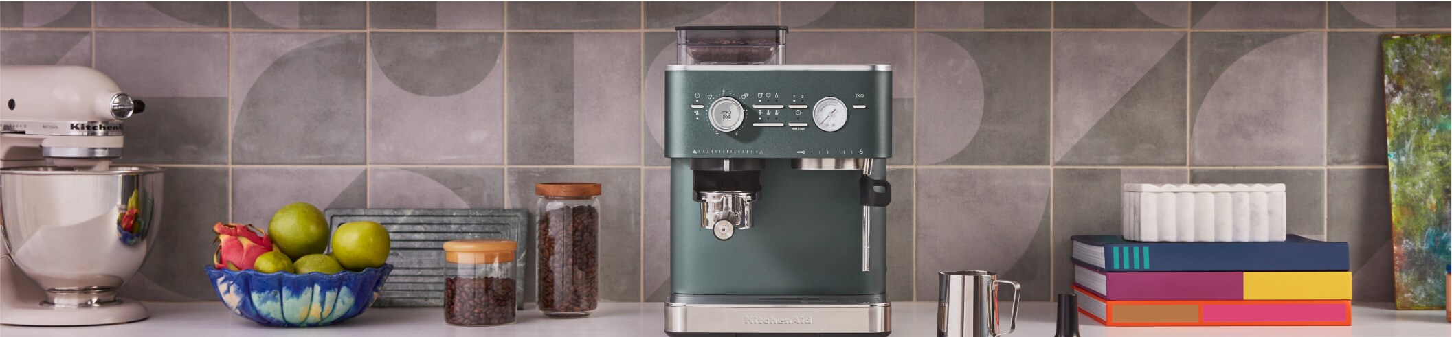 A contemporary KitchenAid Espresso Machine is complemented by a Pitcher, Tamper, coffee beans and fresh fruit.