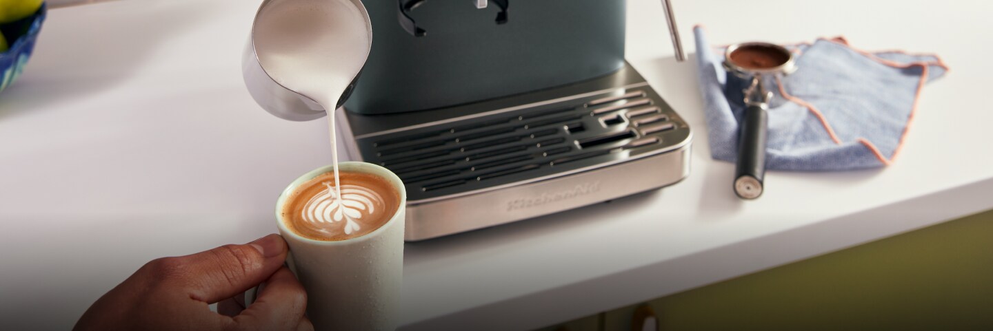 A person pouring steamed milk into a mug of espresso.