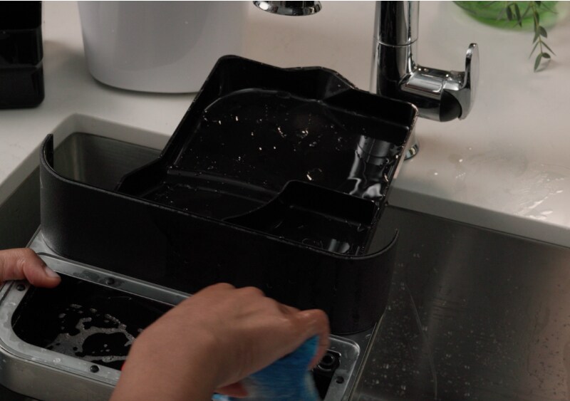 Person cleaning an espresso machine drip tray