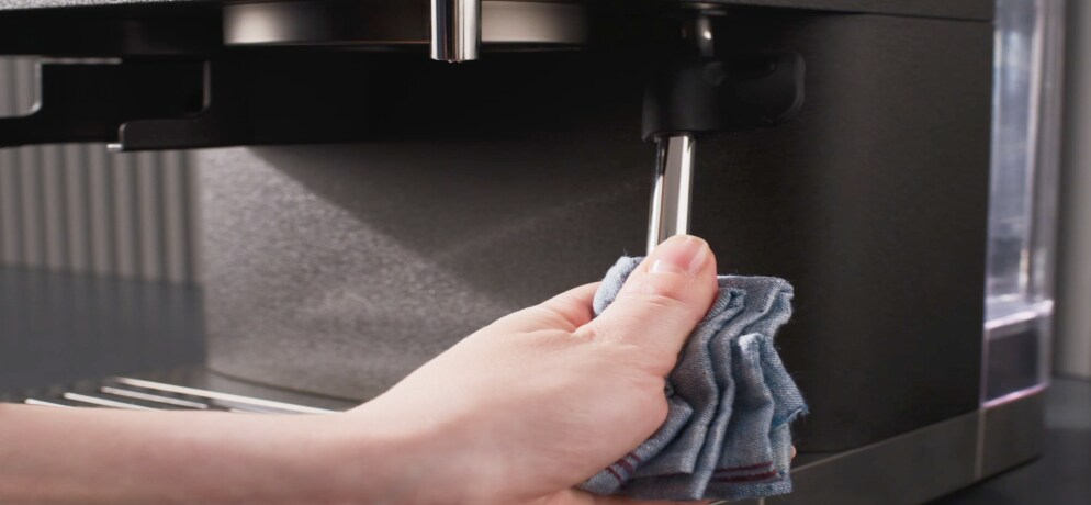 Person cleaning espresso machine steam wand