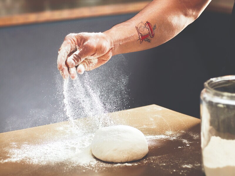 Une personne saupoudrant de la farine sur une boule de pâte