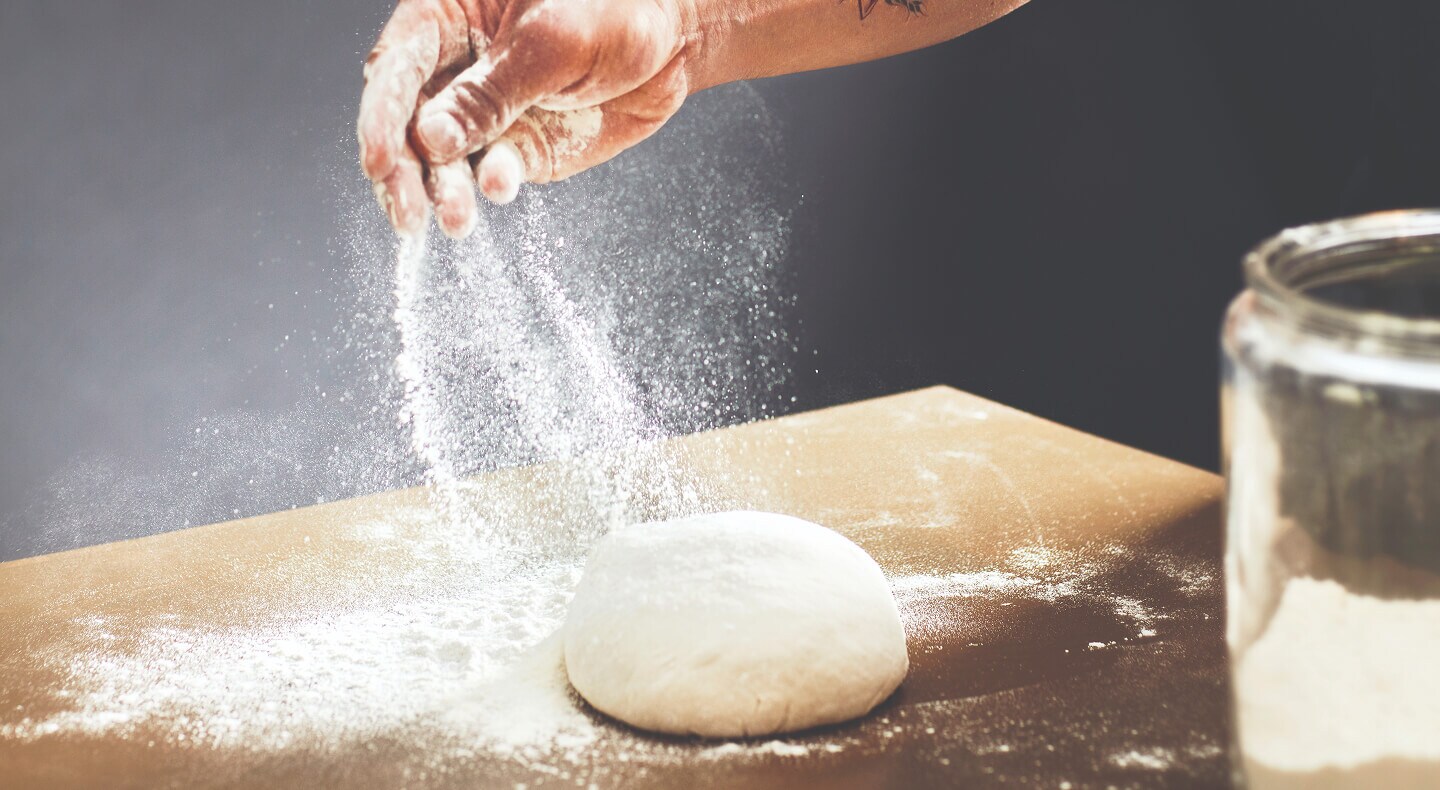 Une personne saupoudrant de la farine sur une boule de pâte