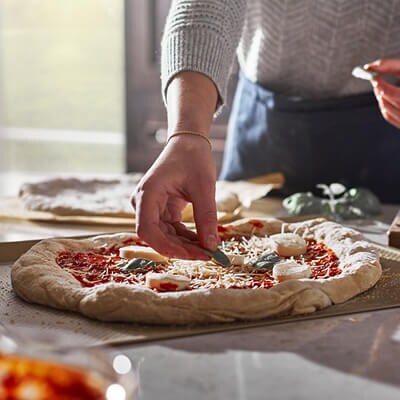 Une personne déposant des ingrédients sur une pizza