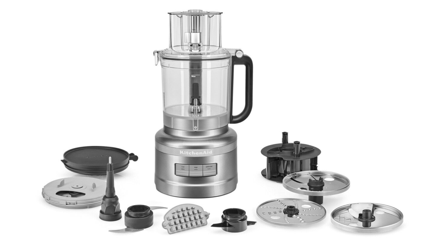 A food processor with its attachments displayed in front it.