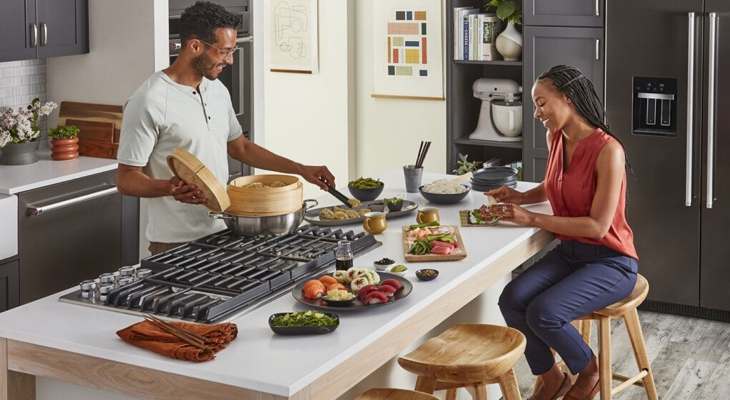 A man and woman preparing various dishes with a stovetop