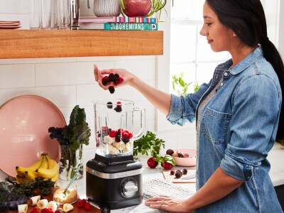 Person filling black blender with ice cream and fruit