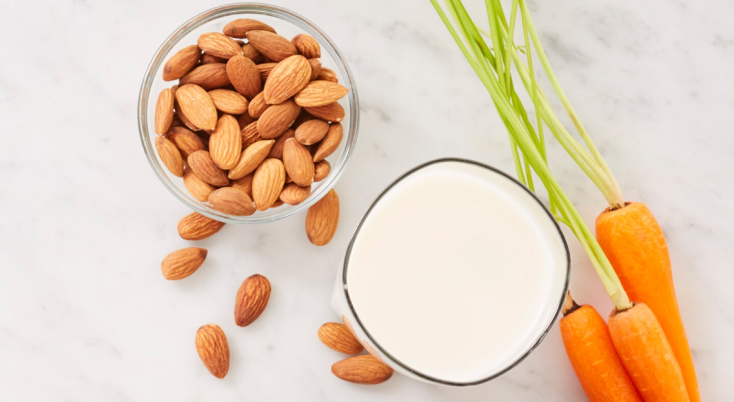 Carrots next to a bowl of almonds and glass of milk