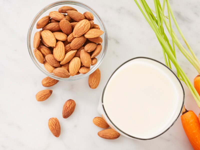 Carrots next to a bowl of almonds and glass of milk