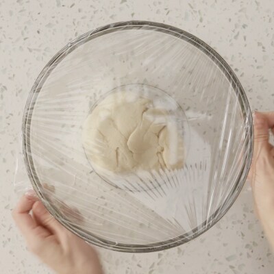 Quelqu'un qui couvre un bol en verre de pâte avec de la pellicule plastique