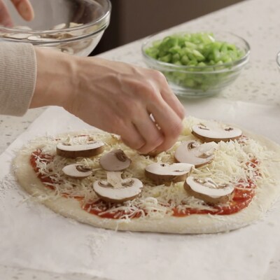 Une personne déposant des ingrédients sur une pizza