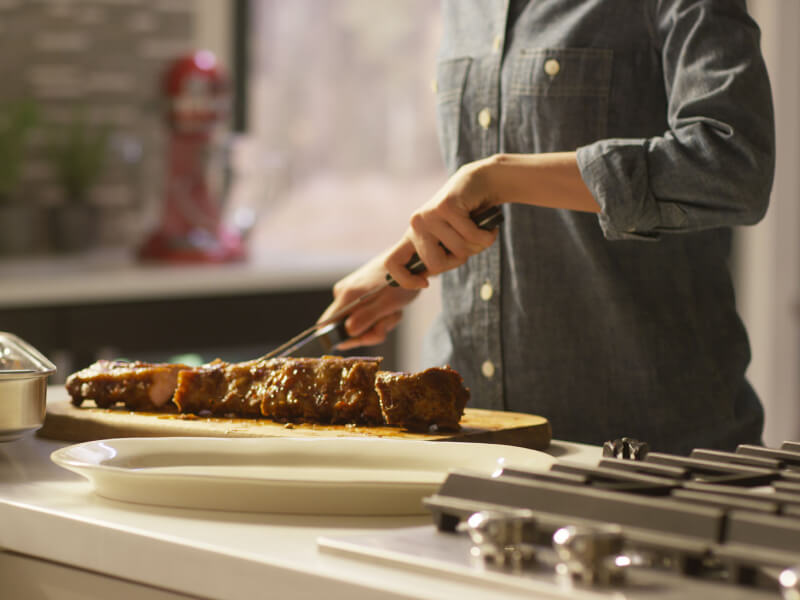 Un cuisinier coupant une plaque de côtes levées tendres.
