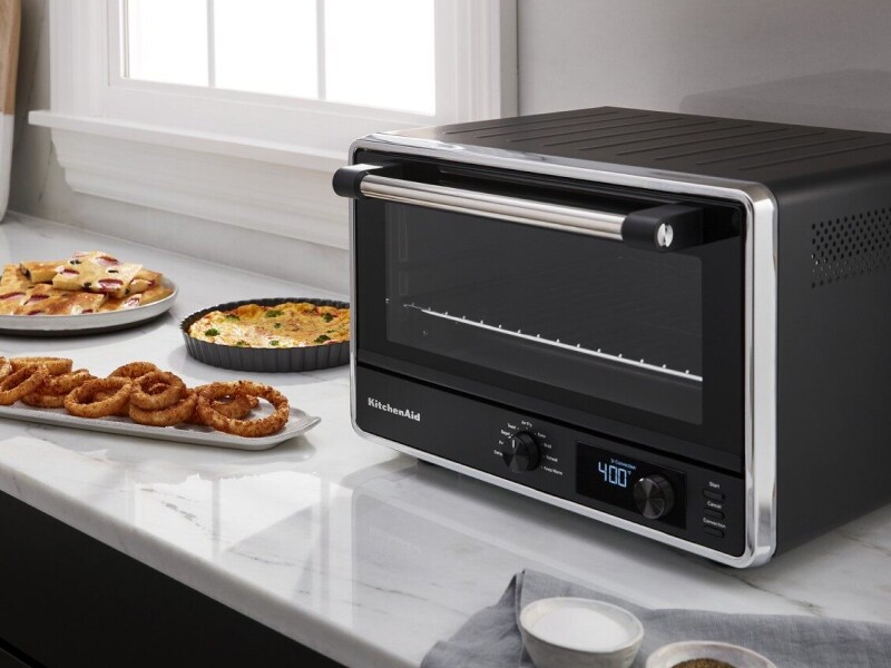 Un four de comptoir noir de la marque KitchenAid sur un comptoir en granit, à côté de plats cuisinés.