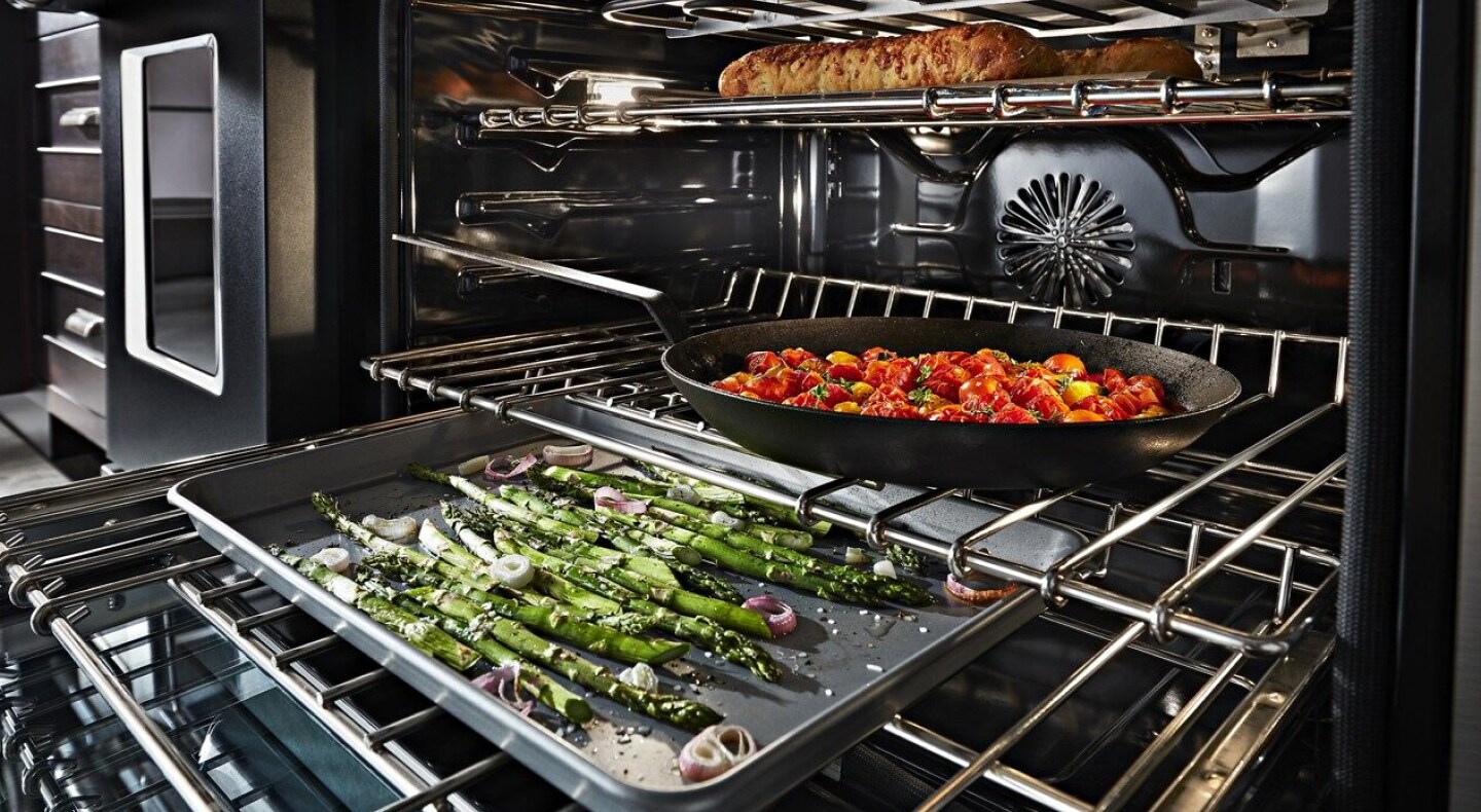 Asparagus, vegetables and bread cooking on separate racks in the oven
