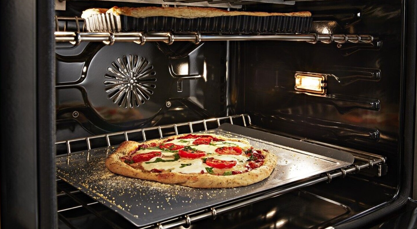 Artisan pizza baking in a convection oven with a dish baking on the rack above