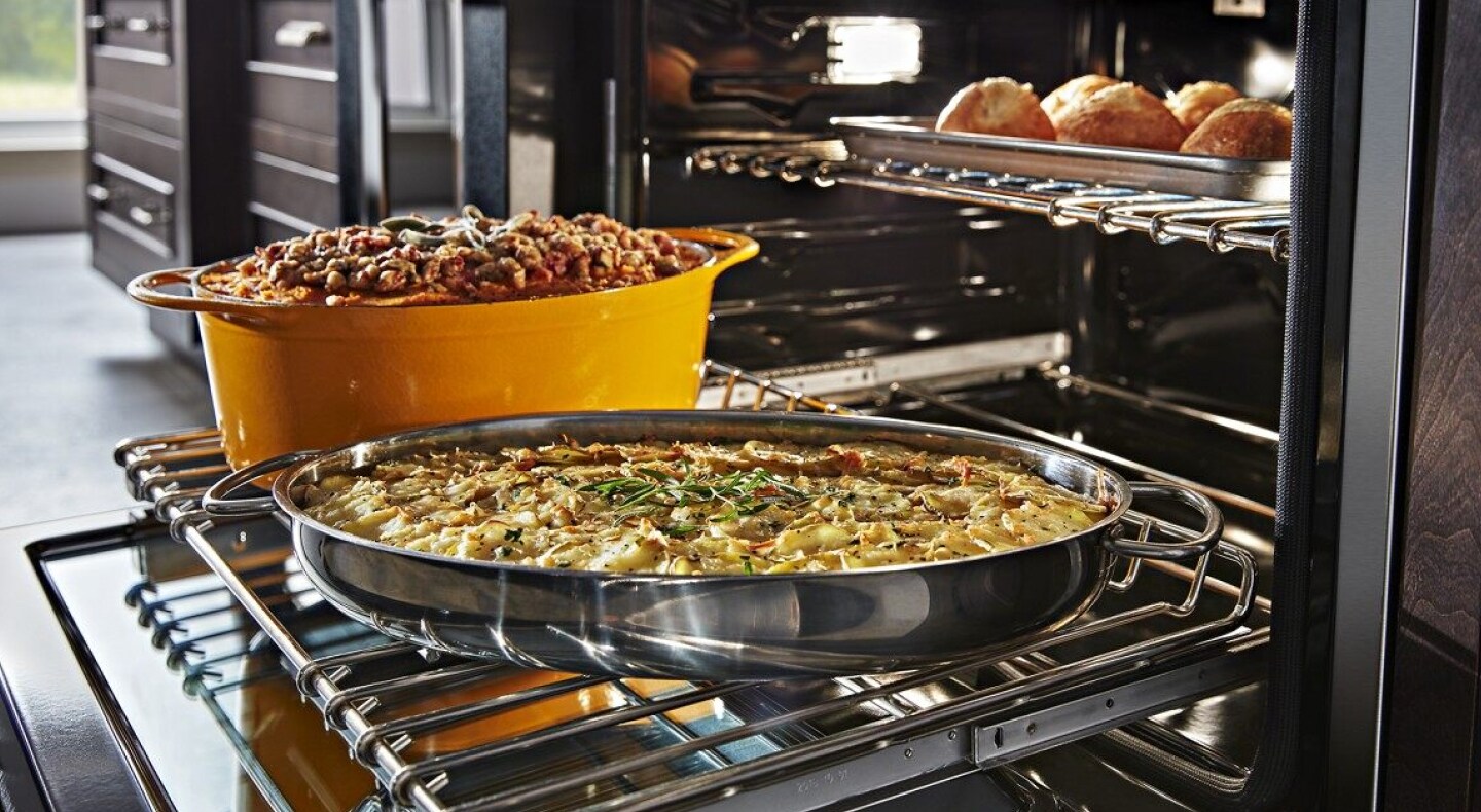 Casseroles sitting on top of an extended bottom oven rack with a dish cooking above