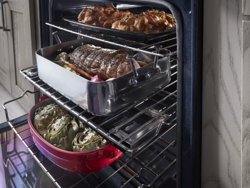 Close-up of two large meat and vegetable dishes sitting on top of extended bottom and top oven racks