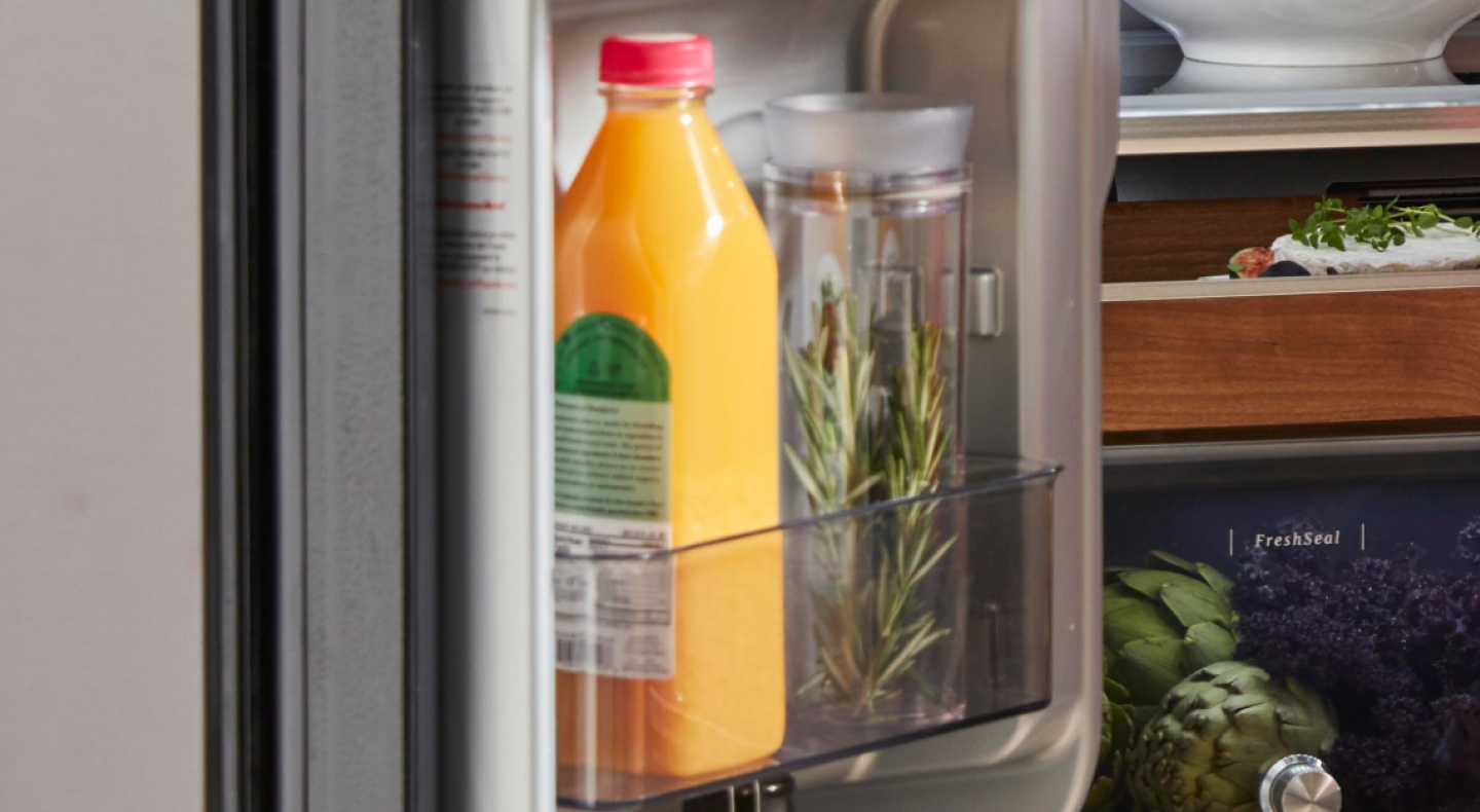 Jar of fresh rosemary in a refrigerator next to a bottle of orange juice