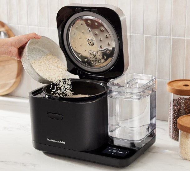 An open Grain and Rice Cooker with a person pouring rice into it.