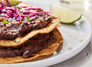 A plate of fish tacos with a side of rice and refried beans.