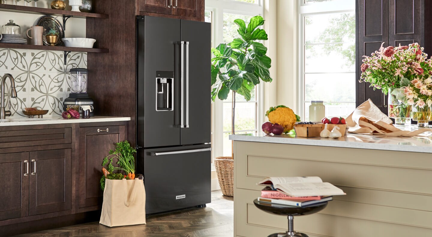 A black stainless steel KitchenAid® French door refrigerator with a bag of fresh produce beside it