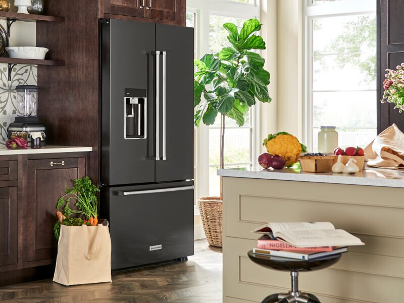 A black stainless steel KitchenAid® French door refrigerator with a bag of fresh produce beside it